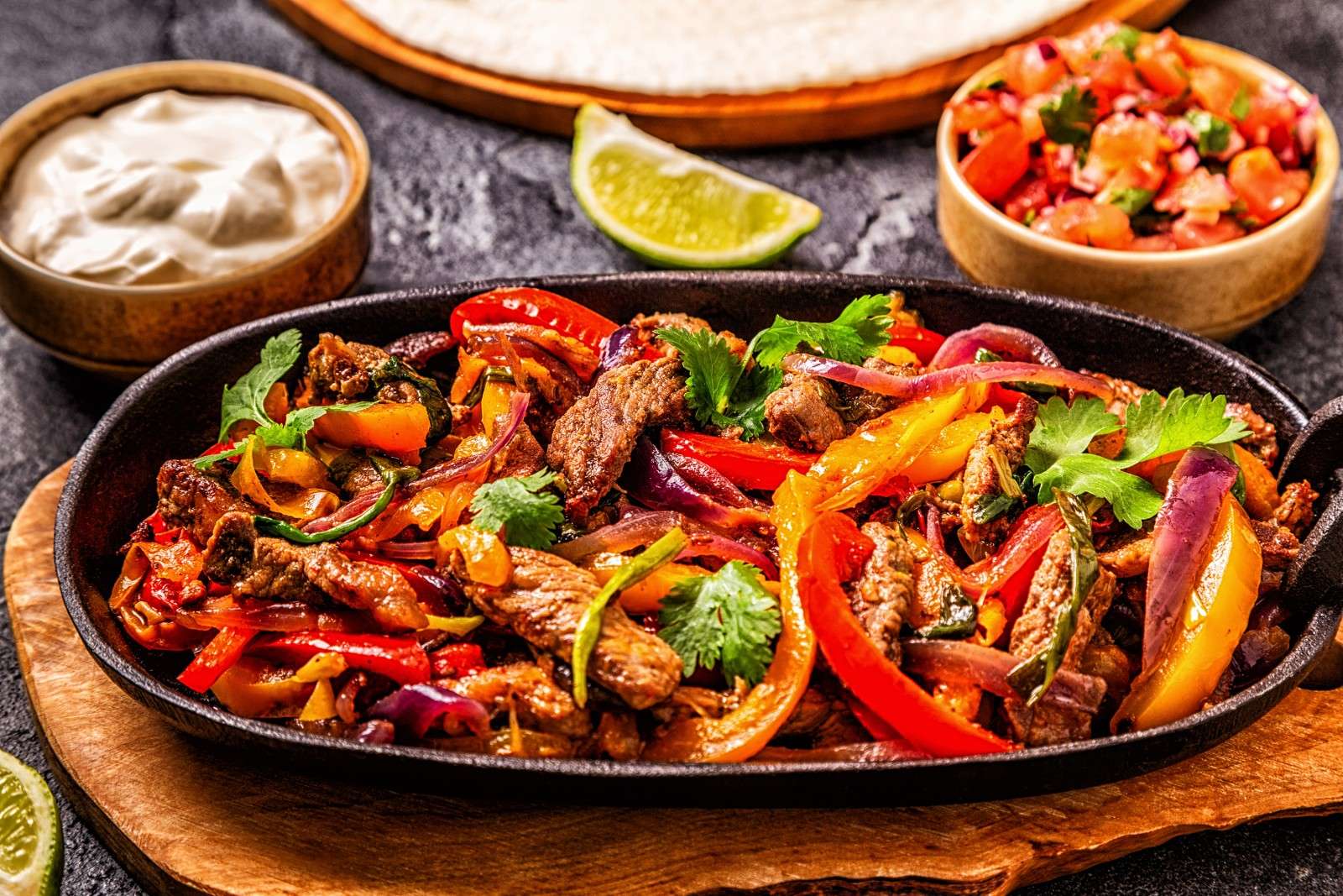 A platter of beef fajitas with salsa and crema
